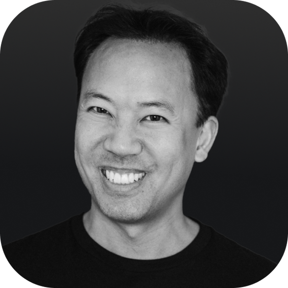 Smiling man with short dark hair in a head-and-shoulders portrait wearing a black shirt on a dark gradient background. Smiling man with short dark hair in a head-and-shoulders portrait wearing a black shirt on a dark gradient background.