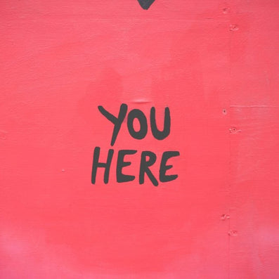 Red painted wall with black hand-lettered text 'YOU HERE'.