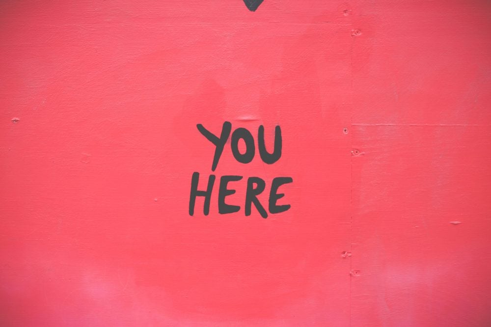 Red painted wall with black hand-lettered text 'YOU HERE'.