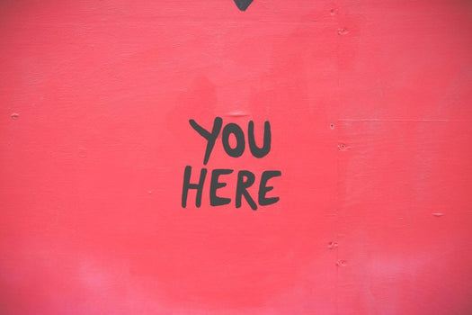 Red painted wall with black hand-lettered text 'YOU HERE'.