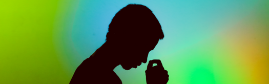 Silhouette of a person holding a small object near their mouth against a colorful gradient background.