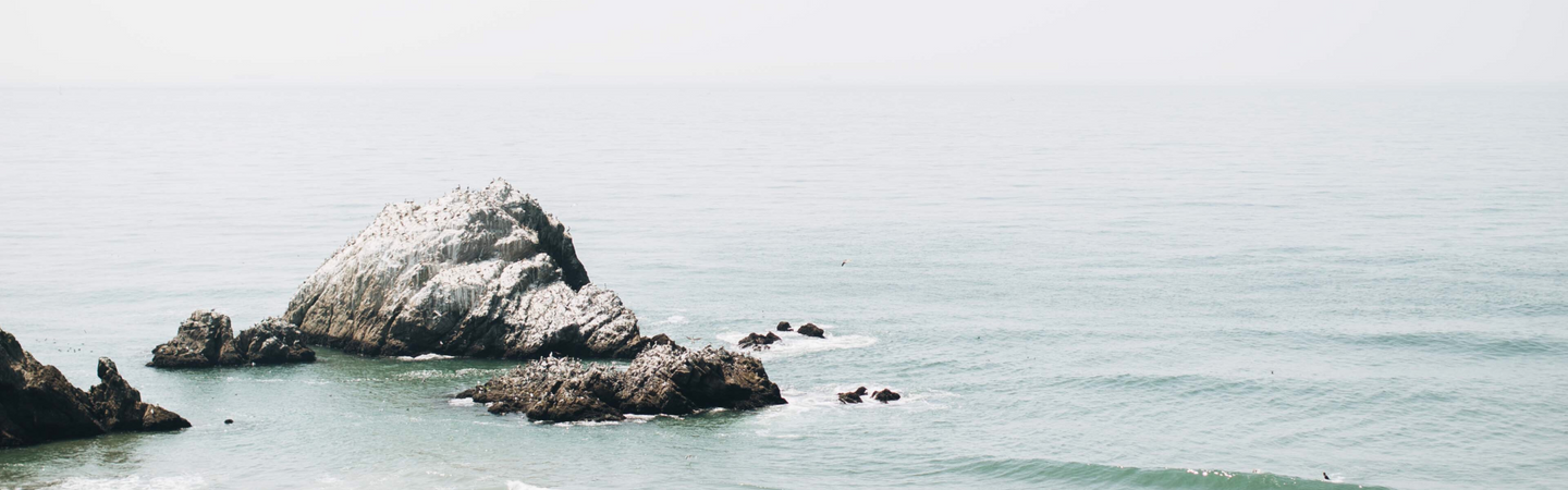 Calm coastal seascape with a rocky outcrop and pale sea under an overcast sky