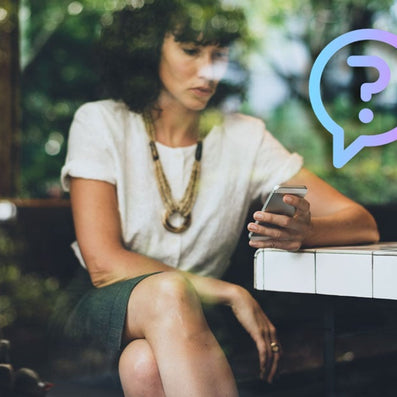 Woman seated at a café table looking at her smartphone, with a translucent question-mark speech bubble overlay
