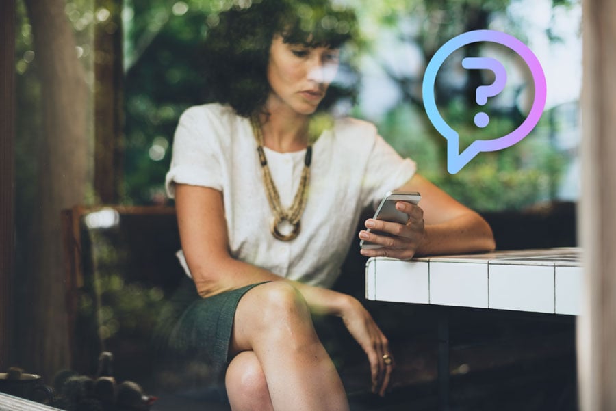 Woman seated at a café table looking at her smartphone, with a translucent question-mark speech bubble overlay