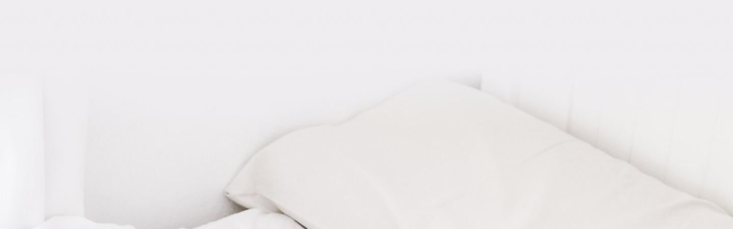 White pillow and blanket on a bed in a bright, minimal bedroom suggesting sleep and relaxation.