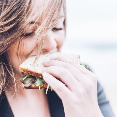 Young woman smiling as she bites a sandwich, close-up of her face and hand