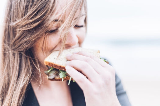 Young woman smiling as she bites a sandwich, close-up of her face and hand
