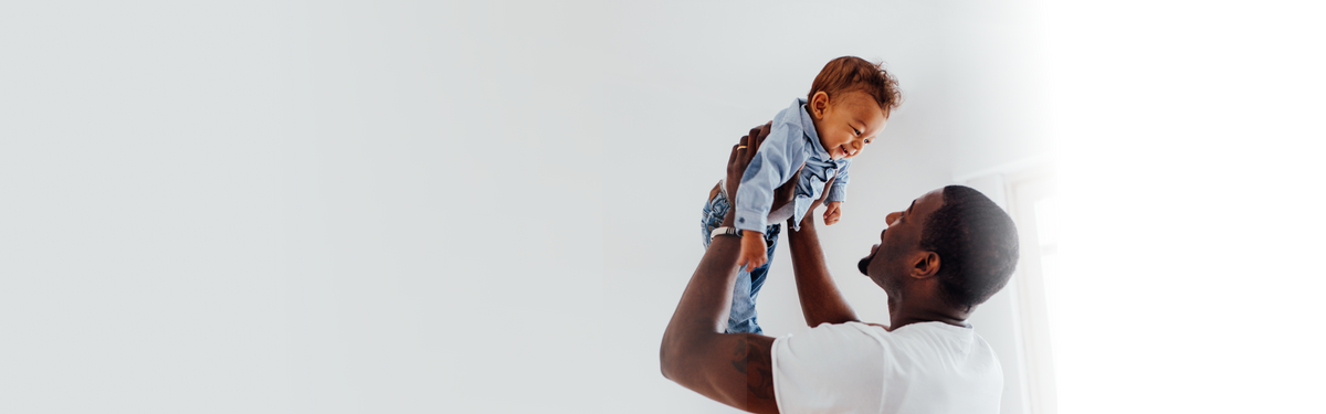 Father lifting a smiling baby in a bright, airy room with a soft gray background