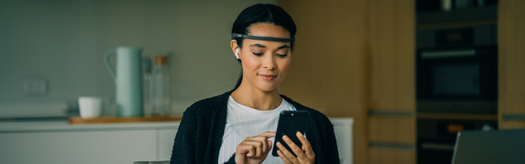 Young woman wearing a headband and earbuds tapping her smartphone in a kitchen setting