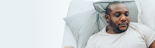 Man lying on bed with pillows, eyes closed, resting and appearing tired