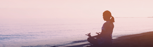 Silhouette of a person seated cross-legged meditating on a beach at sunrise