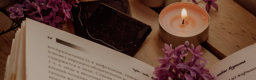 Open book, lit candle, chocolate engraved 'Keep calm and, meditation, mindfulness', purple lilacs on wooden table