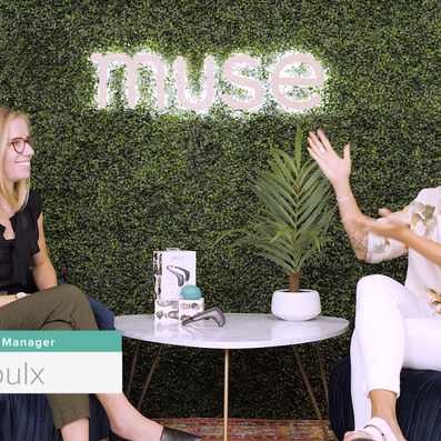 Interview set with Nicole Proulx, Research Engineering Manager, seated with host beneath a neon 'muse' sign