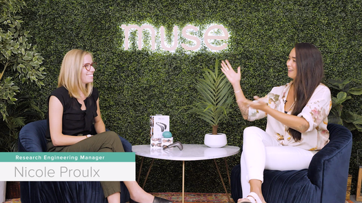 Interview set with Nicole Proulx, Research Engineering Manager, seated with host beneath a neon 'muse' sign