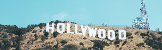 White HOLLYWOOD sign on hillside with radio towers and antennas against a blue sky.