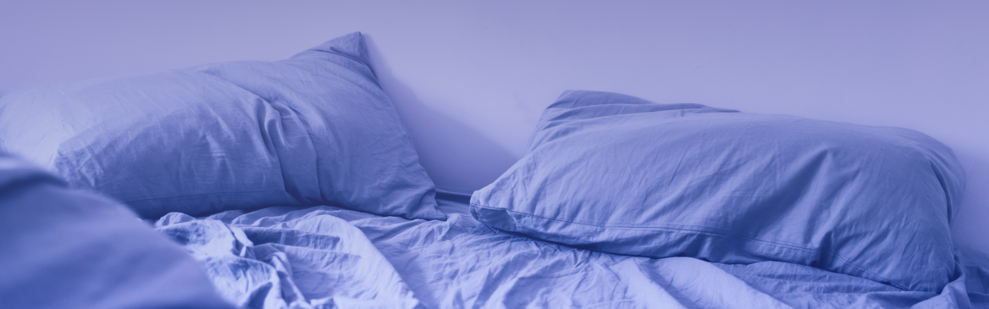 Unmade bed with rumpled light-blue sheets and two pillows in cool blue light
