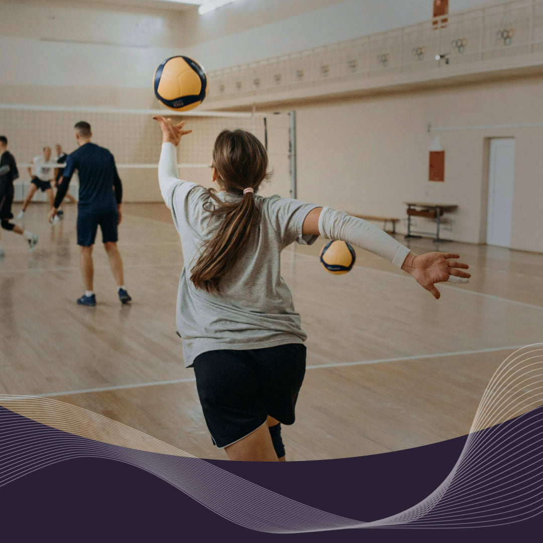 Athlete serving a volleyball in an indoor gym with teammates and a net in the background