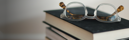 Stack of closed books with reading glasses resting on top, shallow depth of field