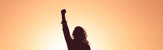 Silhouette of a person raising a fist toward a sunrise, symbolizing empowerment and resilience.