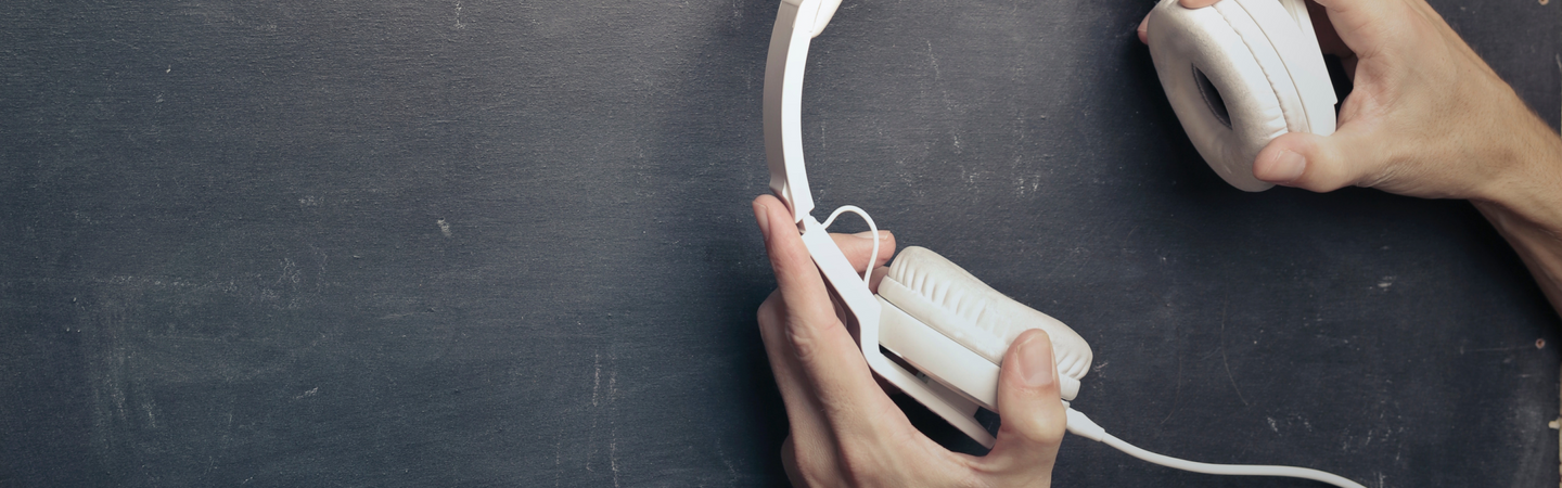 Hands holding white over-ear headphones on a dark textured background