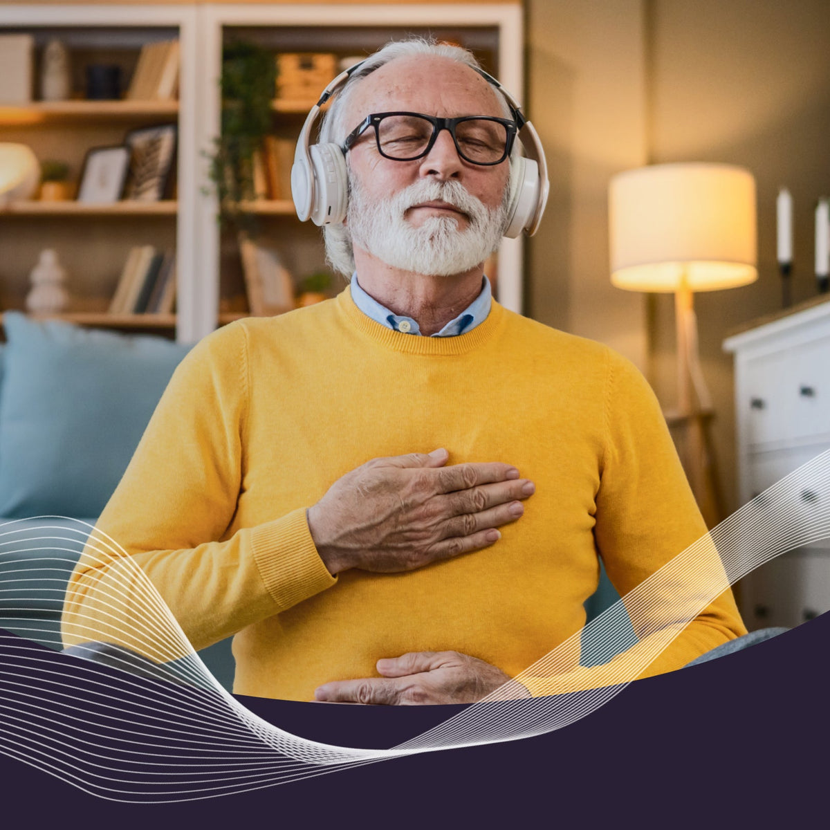 Older man wearing headphones with eyes closed, hand on chest, practicing a breathing exercise in a living room
