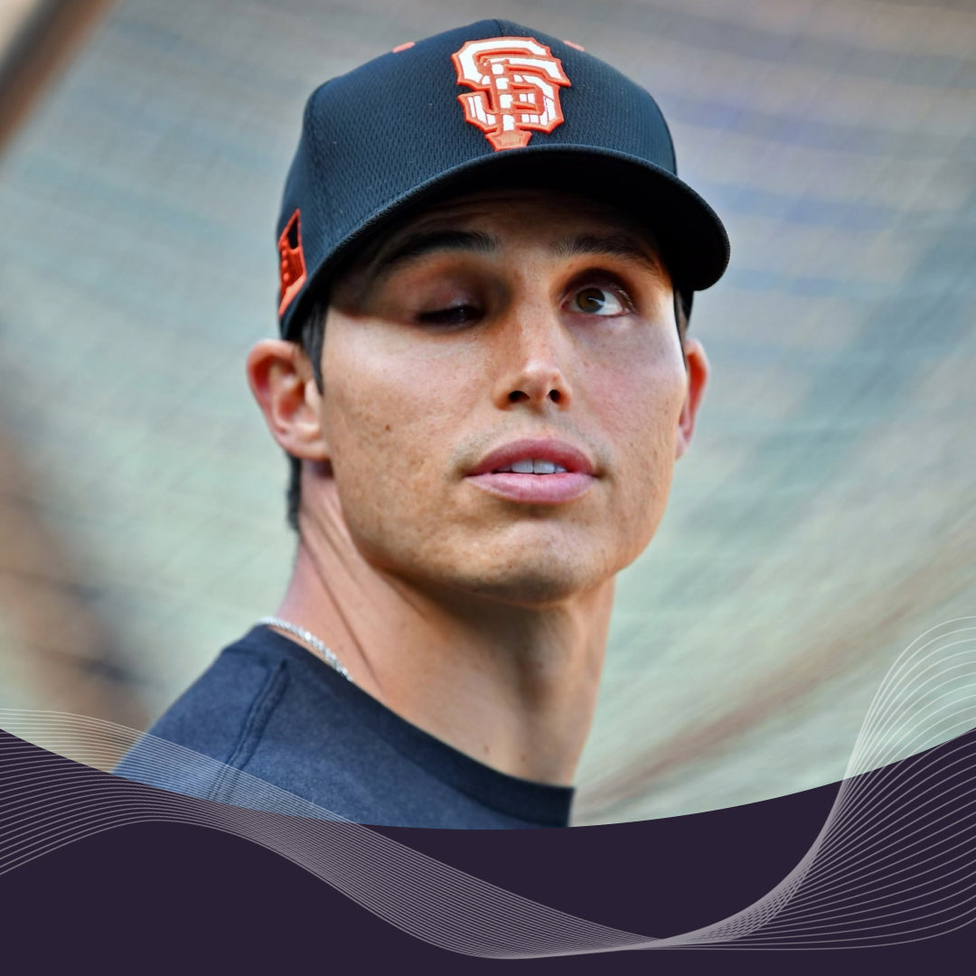 Baseball player glancing to the side on a field, wearing a black cap with orange SF logo, with Muse wave graphic at the bottom